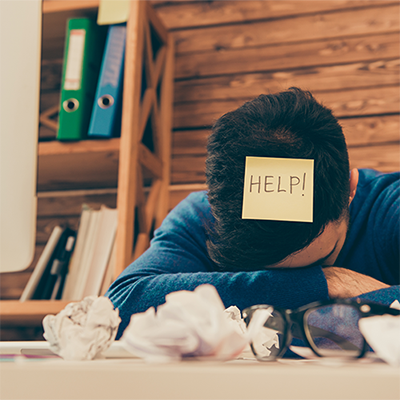 Distressed employee with his head on his hands and a sticky note reading Help!